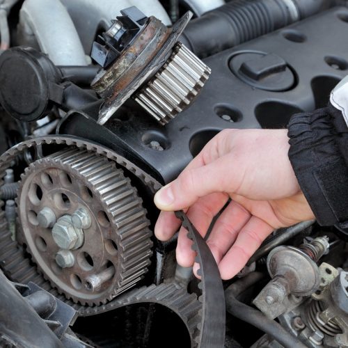 Car mechanic replacing timing belt at camshaft of modern engine